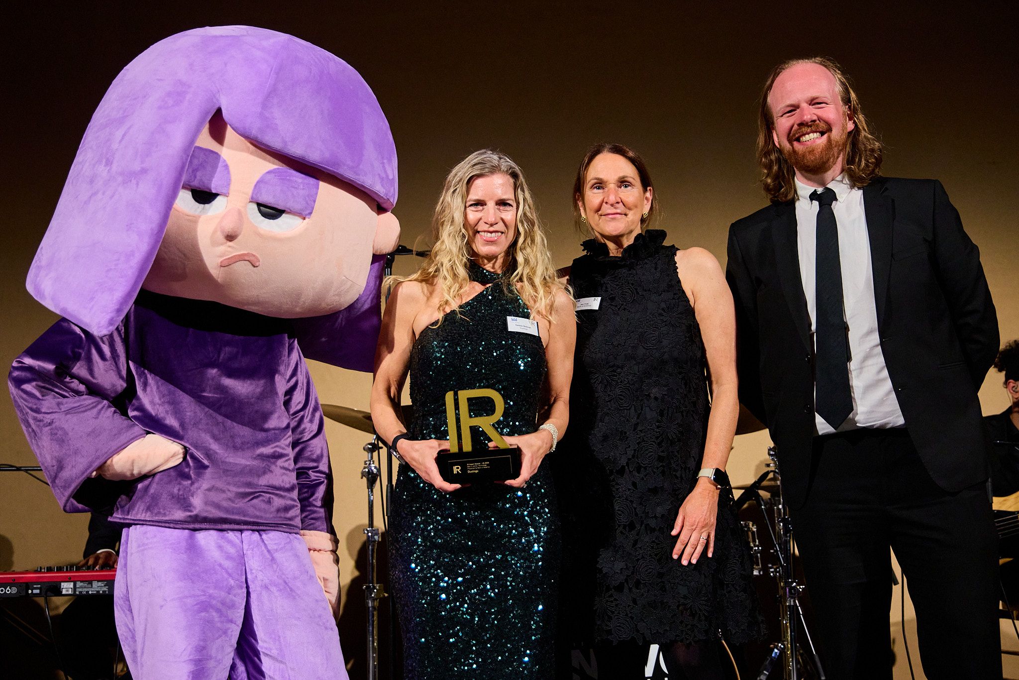 Debbie Belevan picks up a trophy alongside Duolingo's mascot, Lily
